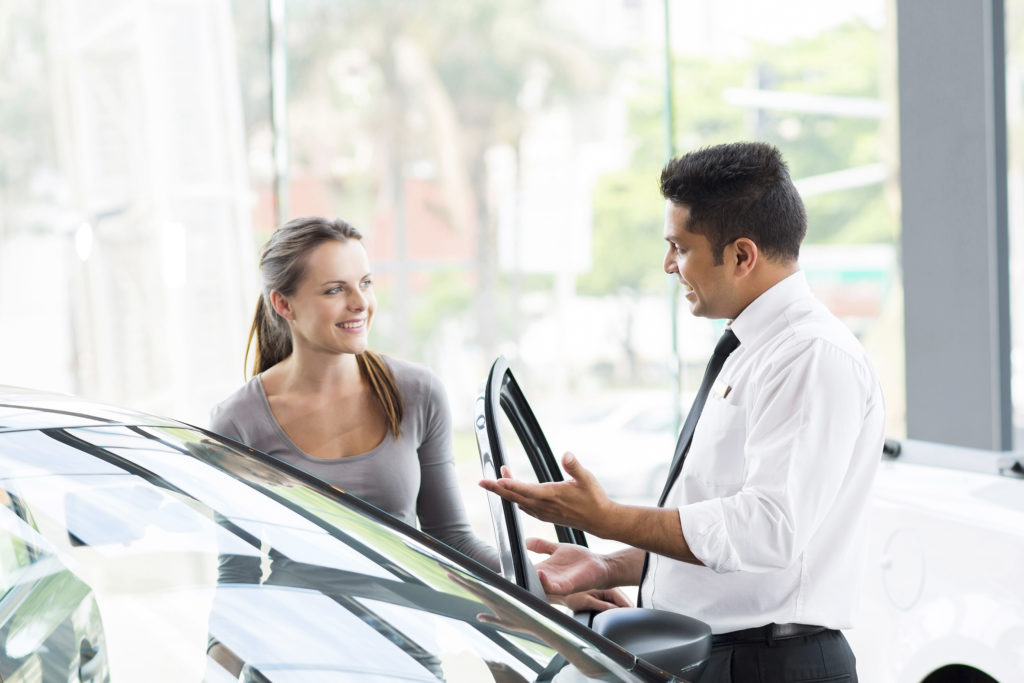 friendly vehicle dealer showing young woman new car